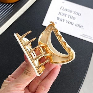 Golden alloy and white acetate square hair claw clip shown in hand with open mechanism