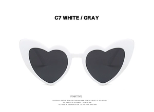 Front detail of heart-shaped sunglasses in white frame with grey lenses and model text C7