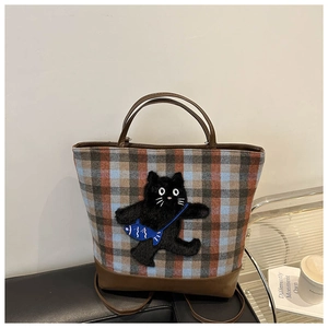 Detail view of plaid wool tote bag with cat embroidery and leather straps on sofa