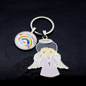 Detail of metal rainbow keychain with Schulkind text and guardian angel charm on dark surface