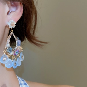 Detailed close-up of blue teardrop pendant earring with white resin flower stud on model