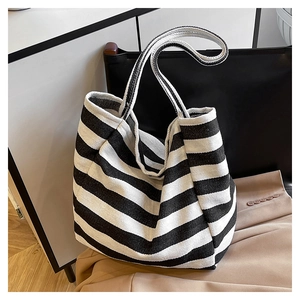 Close-up of a striped canvas tote bag resting on a black leather chair in a minimalist room
