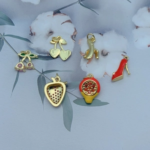 Selection of six gold fruit charms with zircon and enamel on a floral cotton background