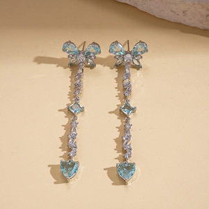 Detail of silver drop earrings featuring zircon bow, tassel and blue heart stones