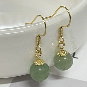 Detail of light green bead earrings with golden floral caps on a ceramic edge
