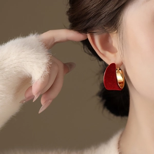 Elegant C-shaped red flocked earrings with gold metal lining worn by a model