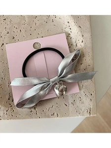 Close-up of black hair tie with silver bow and heart pendant on pink card