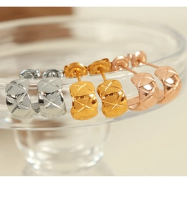 Macro detail of three-color C-shaped quilted stripe earrings on a glass rim