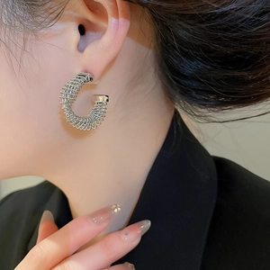 Macro side view of silver spiral C-shaped earrings worn with a black suit jacket
