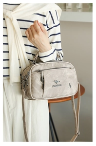 Detail view of beige soft leather handbag featuring multi-layer zipper pockets and kangaroo logo