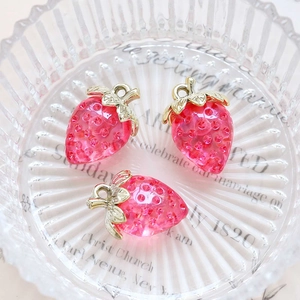 Detailed view of three pink translucent acrylic strawberry charms with gold metal leaves