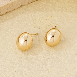 Polished gold irregular oval stud earrings set on a textured beige stone background