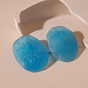 Close-up of blue acrylic stud earrings with textured finish on artistic stone props
