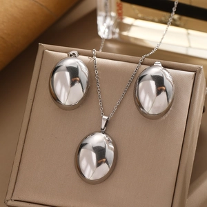Polished silver geometric necklace and oval stud earrings set on a beige jewelry box