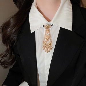 Detail view of a vintage gold tie-shaped brooch with amber stones on a white shirt