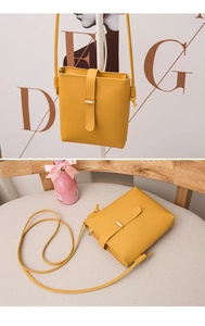 Detail of ginger yellow crossbody bucket bag with gold buckle on soft gray seating