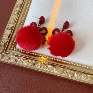 Detailed view of red bow fuzzy pom-pom earrings displayed on a vintage golden frame