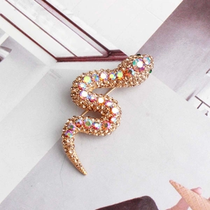 Golden snake brooch with green and champagne crystals on an open magazine backdrop