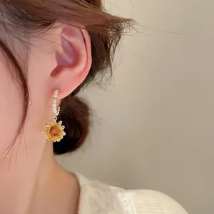 Elegant gold-plated sunflower drop earrings with faux pearls on model's ear