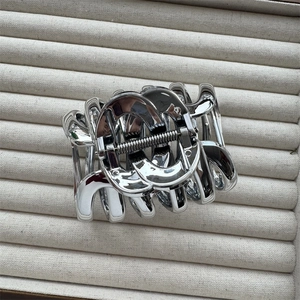 Detailed view of silver metal claw clip with hollow chain design on beige velvet