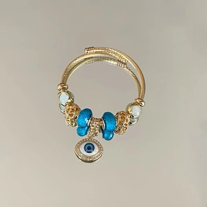 Close-up of golden bangle with blue beads and diamond-encrusted evil eye pendant detail