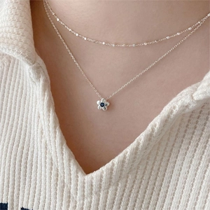Close-up of a double-layer 925 sterling silver daisy necklace with a blue gemstone charm