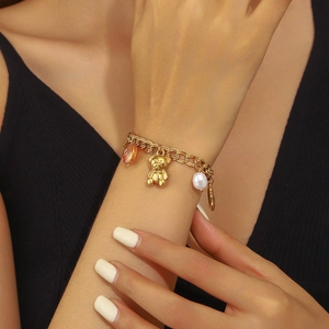 Gros plan d'un bracelet en chaîne plaqué or avec breloques ours, perle et cœur au poignet