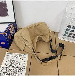 Detail of khaki canvas crossbody bag with adjustable strap and flap on cardboard boxes