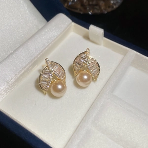 Detailed view of gold plated leaf earrings with zircon accents and round pearl drops