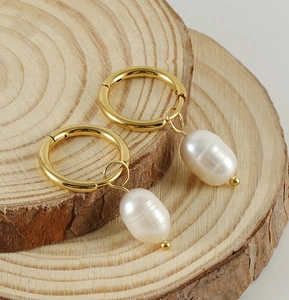 Detail of gold titanium steel hoop earrings with white freshwater pearl pendants on wood