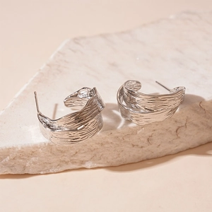 Detailed close-up of C-shaped silver earrings with modern metallic wrinkled texture