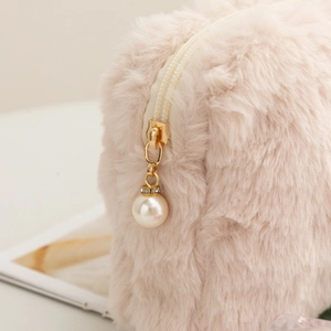 Detail of golden zipper with pearl and rhinestone charm on plush makeup bag