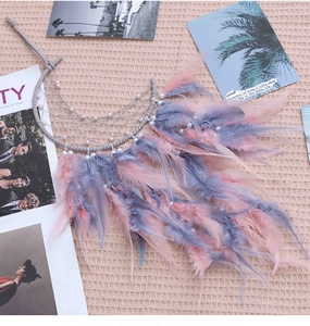Detail of moon-shaped dreamcatcher with pink feathers and pearls on a soft pink texture