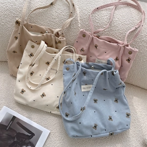 Detailed view of four corduroy tote bags with bear prints in blue, pink, beige, and white
