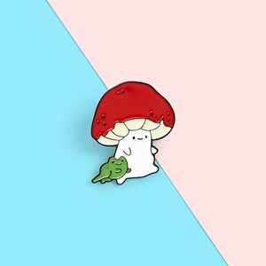 Detail of creative enamel pin showing a red mushroom with a cute green frog