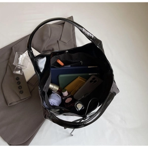 Top-down view of spacious interior of black patent leather tote bag with various essentials