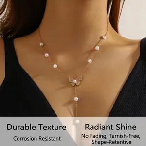 Detailed close-up of a golden butterfly necklace with pink enamel and white pearls on a model