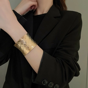 Detail of wide gold cuff bracelet featuring woven texture on a model wearing black
