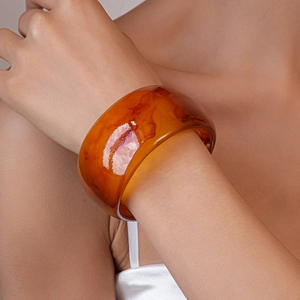 Detail shot of wide amber resin bangle with semi-transparent swirl textures on wrist