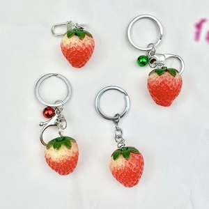 Detail shot of four strawberry keychains with green leaves and bells on white background