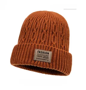 Detailed texture of orange knit beanie featuring a cable knit pattern and leather patch