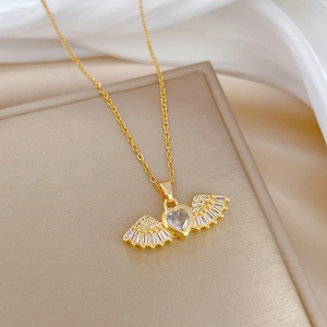 Detailed close-up of golden angel wing necklace with heart-shaped zircon on silk fabric