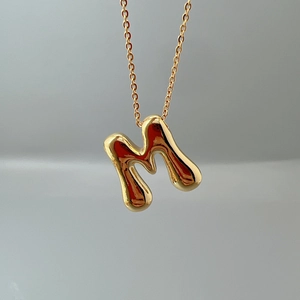 Macro view of gold lava-textured letter M pendant on a delicate link chain necklace