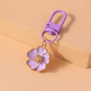 Close-up of purple flower keychain with gold trim on a decorative pink pedestal