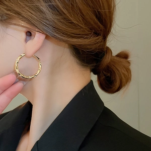 Close-up of golden irregular geometric hoop earring with textured finish on model
