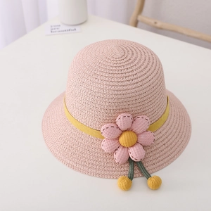 Close-up of pink woven straw hat featuring floral decoration and yellow pom-poms