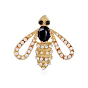 Macro shot of gold bee brooch detailing white pearls and large black gemstones