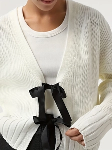 Dettaglio del cardigan in maglia bianca con fiocco di nastro nero e trama fine