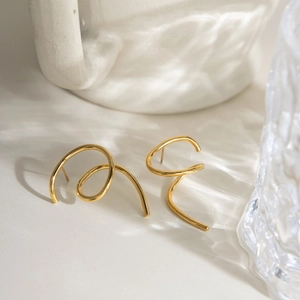 Macro shot of gold minimalist spiral earrings on a rippled light surface