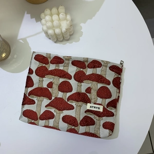 Close-up of mushroom pattern cosmetic bag with red zipper and brand logo detail